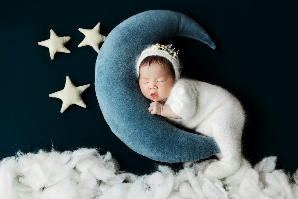 a baby sleeping on a stuffed blue moon toy