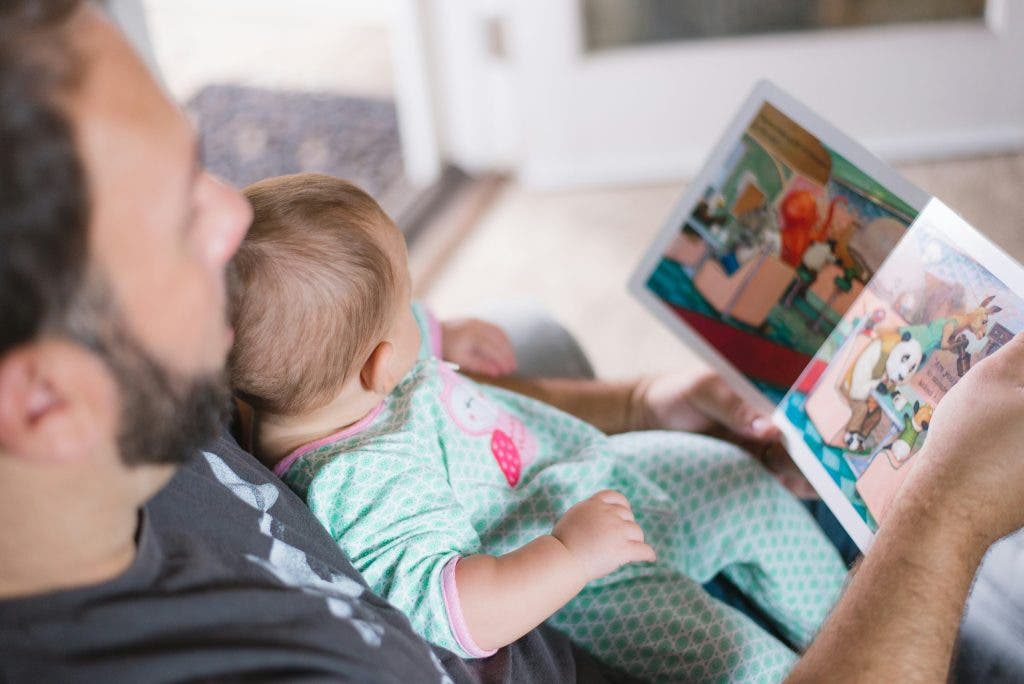 father carrying his baby while reading a book out loud