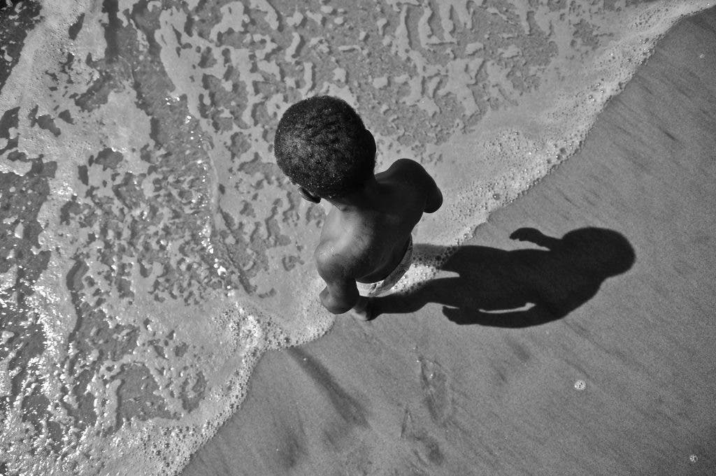 black and white photo of kid meeting wave at the beach