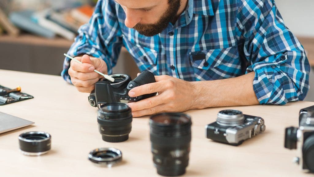 Maintenance of photo camera at workshop. Photographer cleaning photocamera light sensor. Professional photographing equipment care, technology, hobby concept