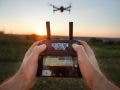 Point of view shot of man holding remote controller with his hands and taking aerial photo video. Copter is flying on background. POV - drone hovers in front of the pilot on suset. No face