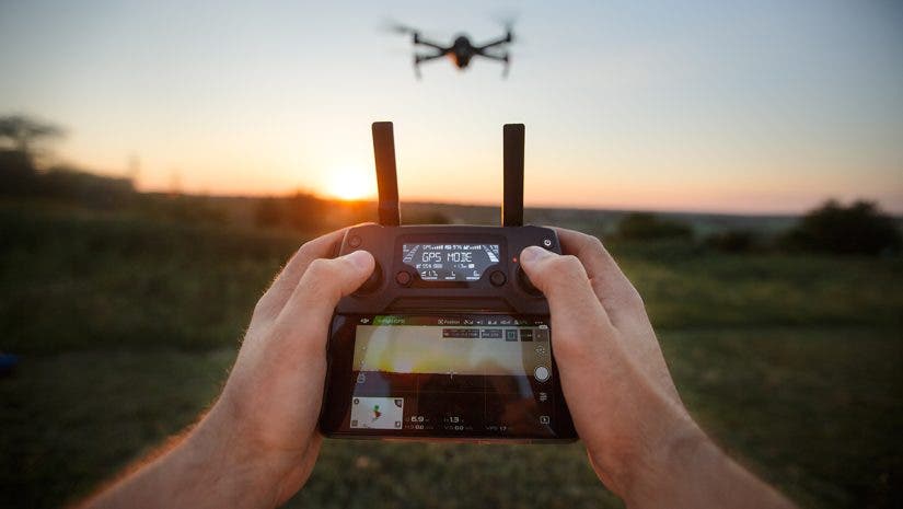 Point of view shot of man holding remote controller with his hands and taking aerial photo video. Copter is flying on background. POV - drone hovers in front of the pilot on suset. No face