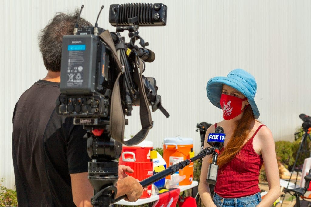 a cinematographer holding a cinematic camera interviewing a girl wearing a mask and hat