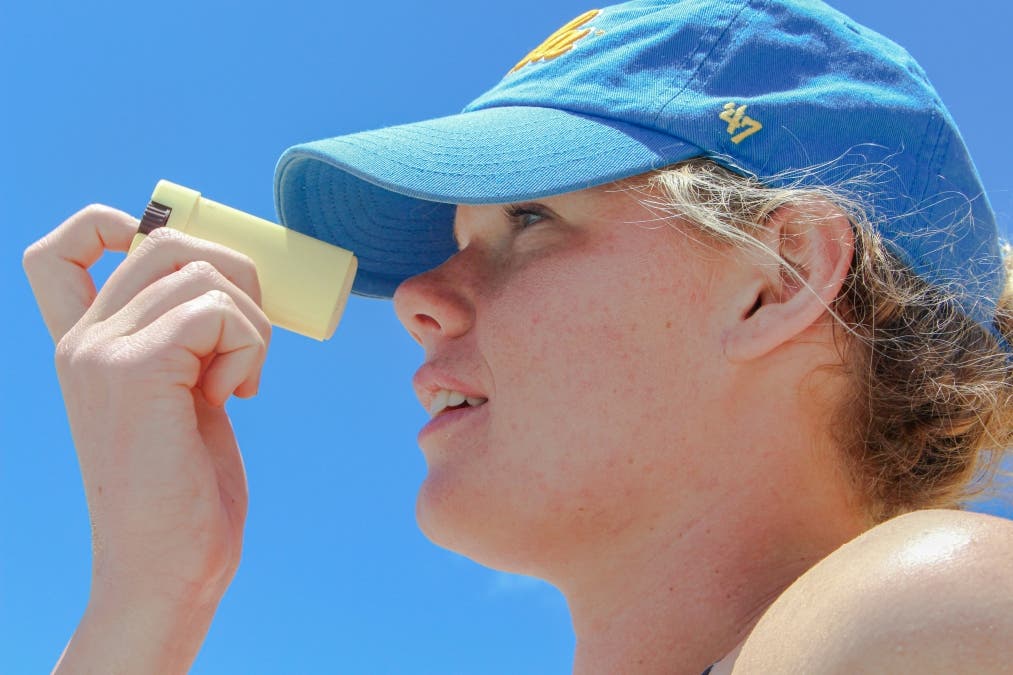 person putting on sunscreen wearing a blue cap