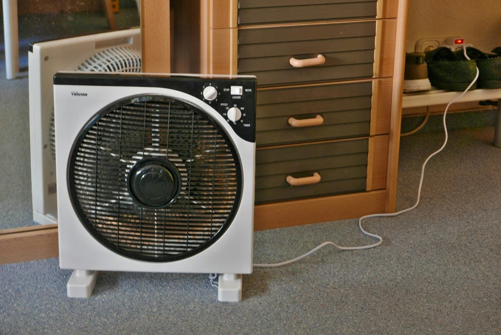 an electric fan on the floor beside a drawer during the summer