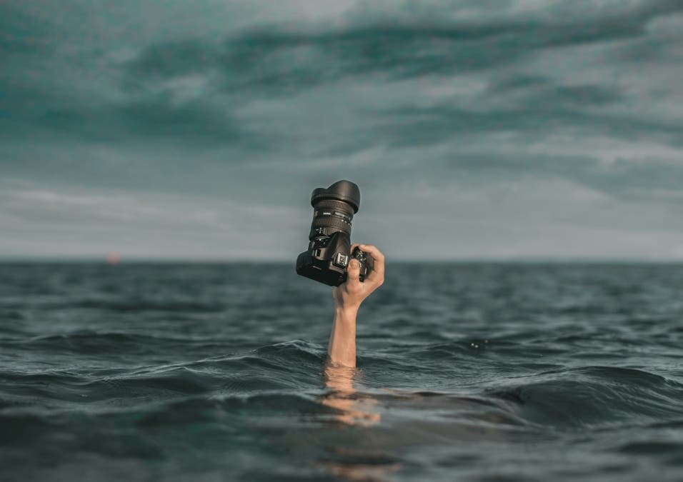 hand holding DSLR camera above the ocean surface