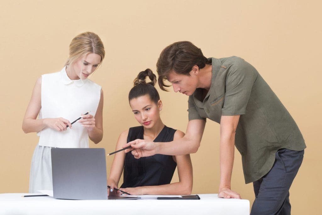 Flat light on three people looking at a laptop, one of them is seated.