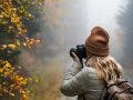 Woman with camera taking picture of autumn leaf. Tourist hiking