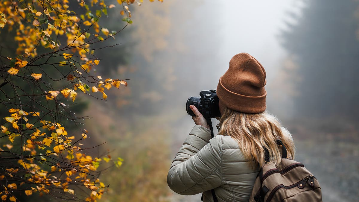 Woman with camera taking picture of autumn leaf. Tourist hiking