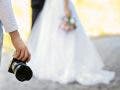 Professional photographer with camera and wedding couple, outdoors
