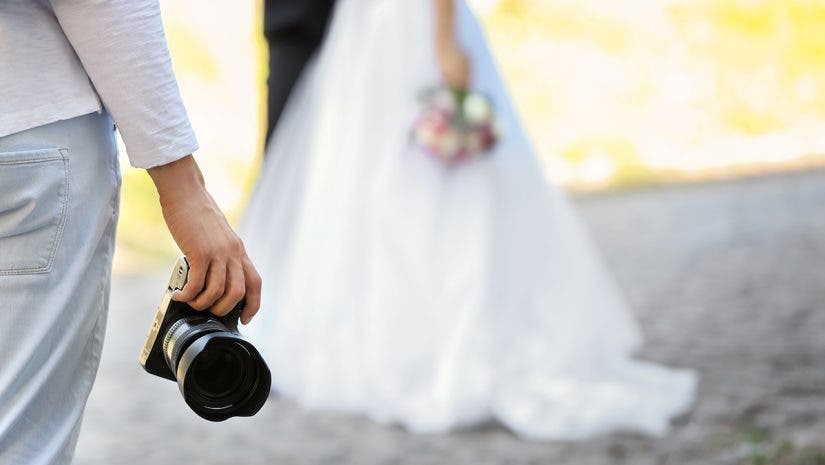 Professional photographer with camera and wedding couple, outdoors