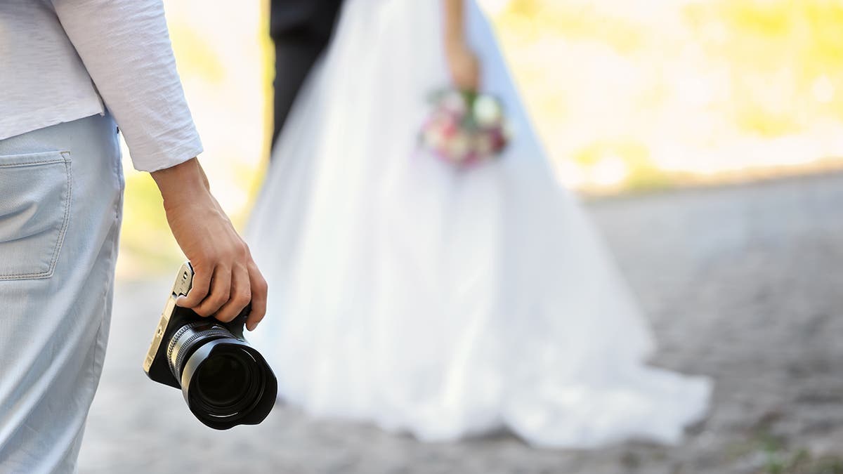 Professional photographer with camera and wedding couple, outdoors