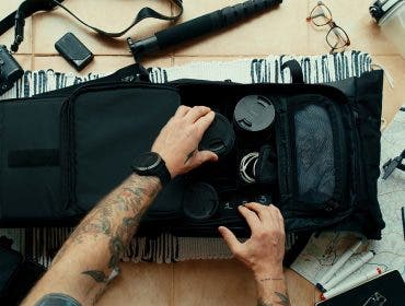 Professional travel blogger and photographer packs smart backpack with equipment and photo gear. Social media influencer top view on suitcase with lens, videocamera and camera,amateur drone and gimbal