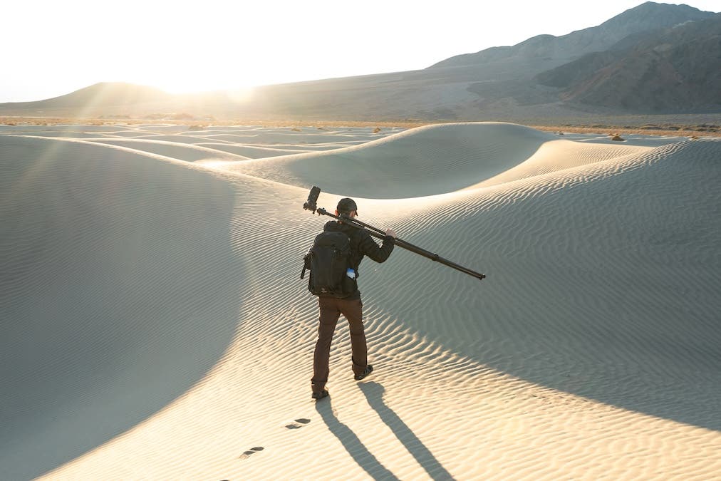 man carrying photography gear through sand dunes