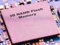 A macro close-up of a square memory chip labeled '3D NAND Flash Memory' mounted on a blue printed circuit board with visible gold contacts.