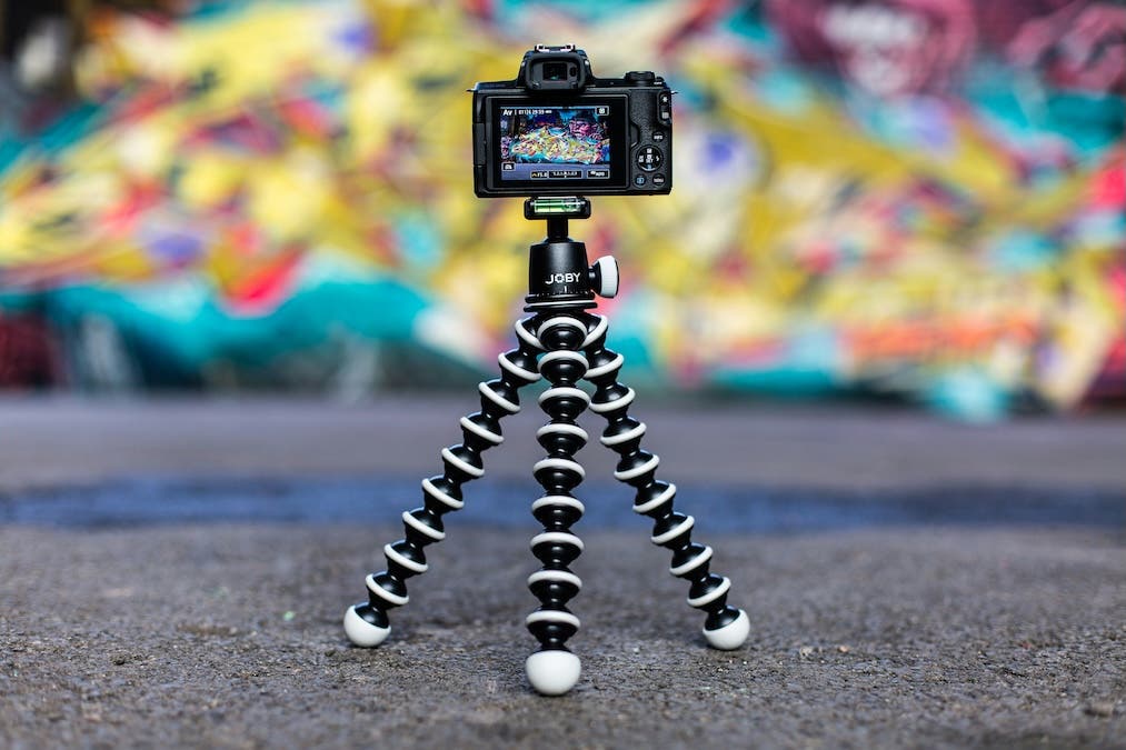 tripod holding a camera in front of bright colored wall