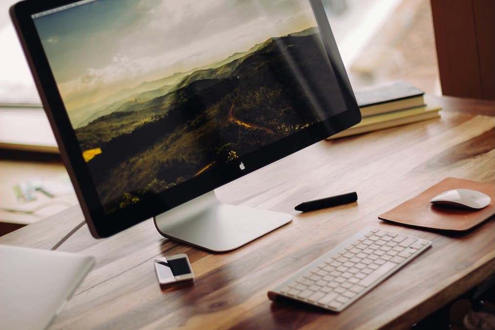 picture of wooden desk with Mac monitor and magic keyboard
