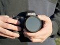 man wearing black sweater holds Nikon camera in both hands