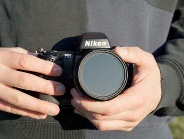 man wearing black sweater holds Nikon camera in both hands