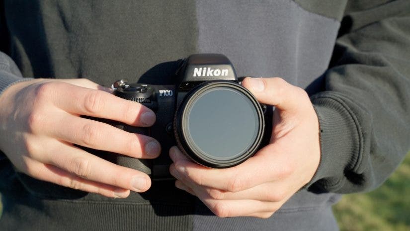 man wearing black sweater holds Nikon camera in both hands