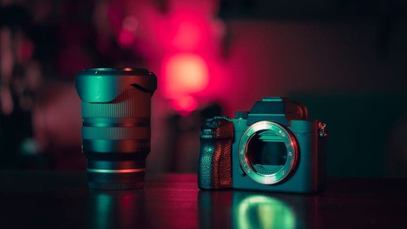 A professional mirrorless camera body and a high-end lens standing on a dark surface, illuminated by moody pink and teal studio lighting to illustrate the concept that the right gear pays for itself.