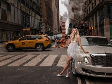 An editorial-style wedding portrait of a bride in a white fringe dress leaning against a luxury sedan on a busy New York City street with a yellow taxi in the background, demonstrating the urban flair of a wedding photography side hustle. Photo by Susan Stripling.