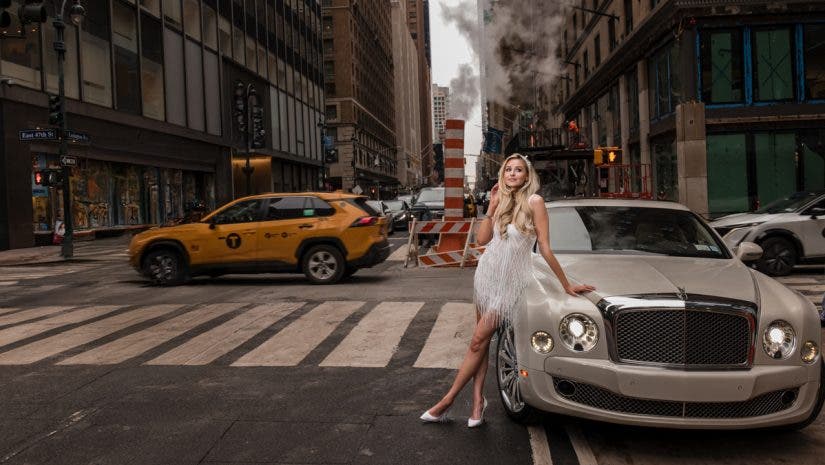 An editorial-style wedding portrait of a bride in a white fringe dress leaning against a luxury sedan on a busy New York City street with a yellow taxi in the background, demonstrating the urban flair of a wedding photography side hustle. Photo by Susan Stripling.