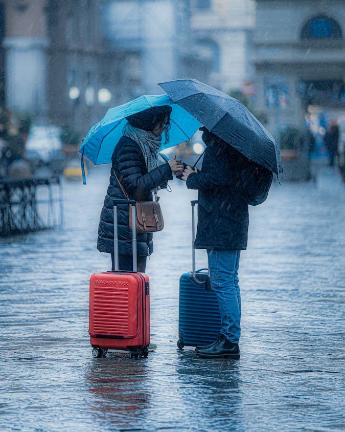 a couple stands underneath umbrellas with their luggage in rainy Florence Italy