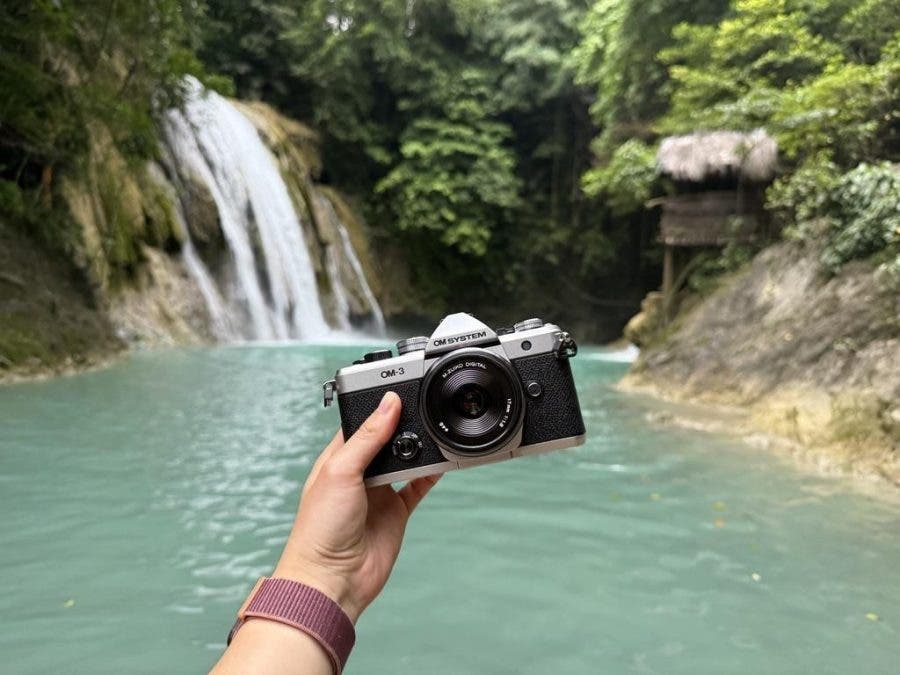 holding OM-SYSTEM OM-3 camera in front of a waterfall
