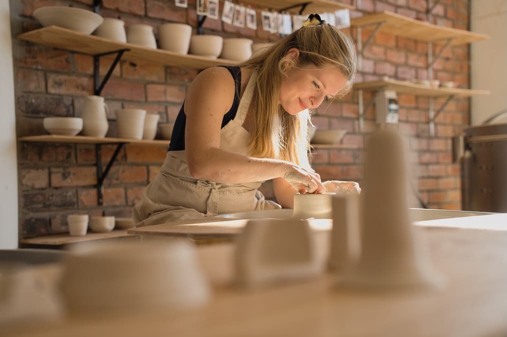 a woman smiles as she looks down on her pottery machine work