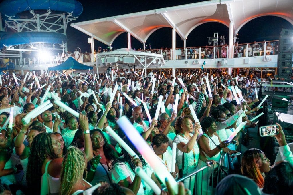 A vibrant nighttime shot of a crowd in white attire during a cruise ship deck party. The scene is illuminated by off-camera Flashpoint speedlights, which freeze the motion of the guests as they wave glowing LED sticks, ensuring the white clothing pops against the dark sky and ship structures.