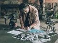 a man is looking down on a desk writing his shot list with photos scattered