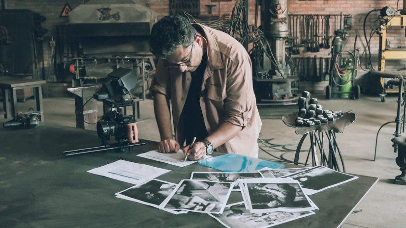 a man is looking down on a desk writing his shot list with photos scattered