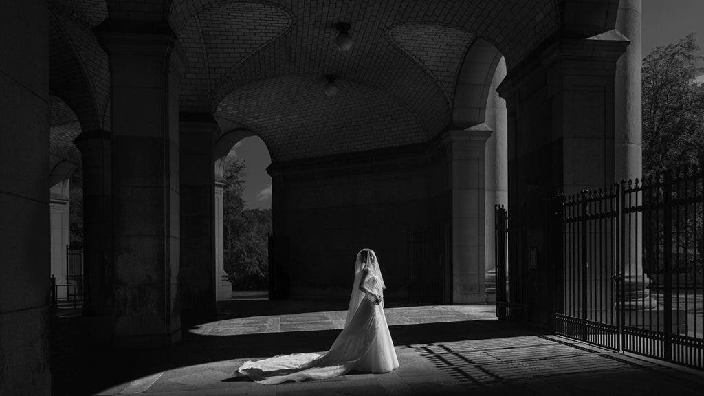 a bride wearing a wedding gown stands in empty hall, black and white wedding photography image