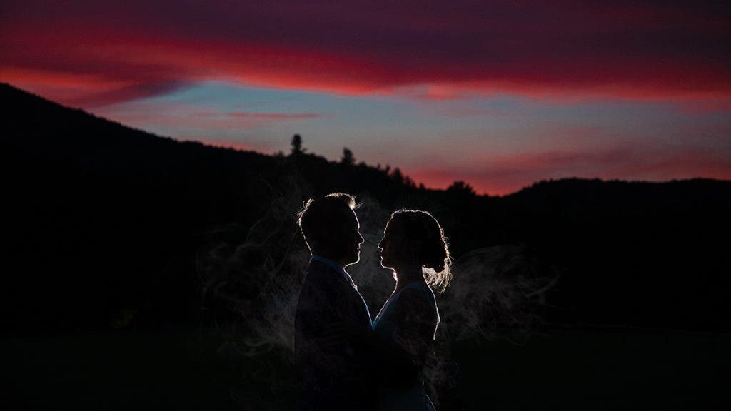 a silhouetted couple stands with a burning sunset in the background