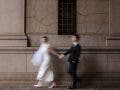 An artistic, motion-blurred shot of a bride and groom holding hands and walking quickly past a textured stone wall; a dynamic style that generates word of mouth, photographed by Susan Stripling.