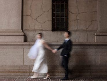 An artistic, motion-blurred shot of a bride and groom holding hands and walking quickly past a textured stone wall; a dynamic style that generates word of mouth, photographed by Susan Stripling.