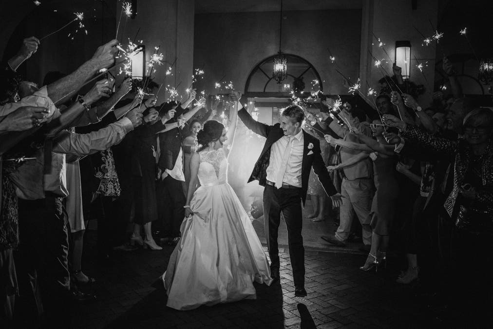 bride and groom walk past guests holding sparklers, black and white photo