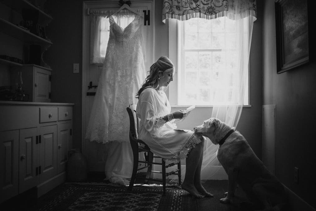 bride sits in front of her wedding dress while a dog rests its head on her knees