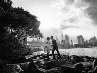 bride holds her dress up as she kisses groom on a rocky riverbank