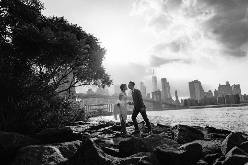 bride holds her dress up as she kisses groom on a rocky riverbank