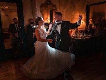 groom in tuxedo and bride in wedding dress happily dance around holding drinks