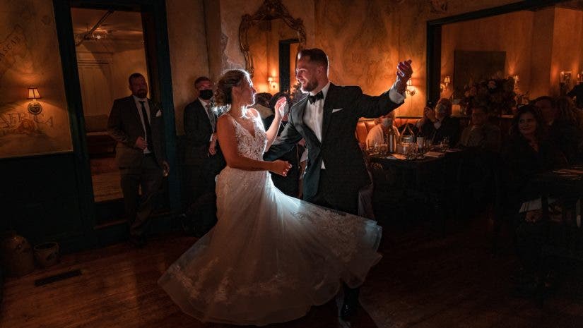 groom in tuxedo and bride in wedding dress happily dance around holding drinks
