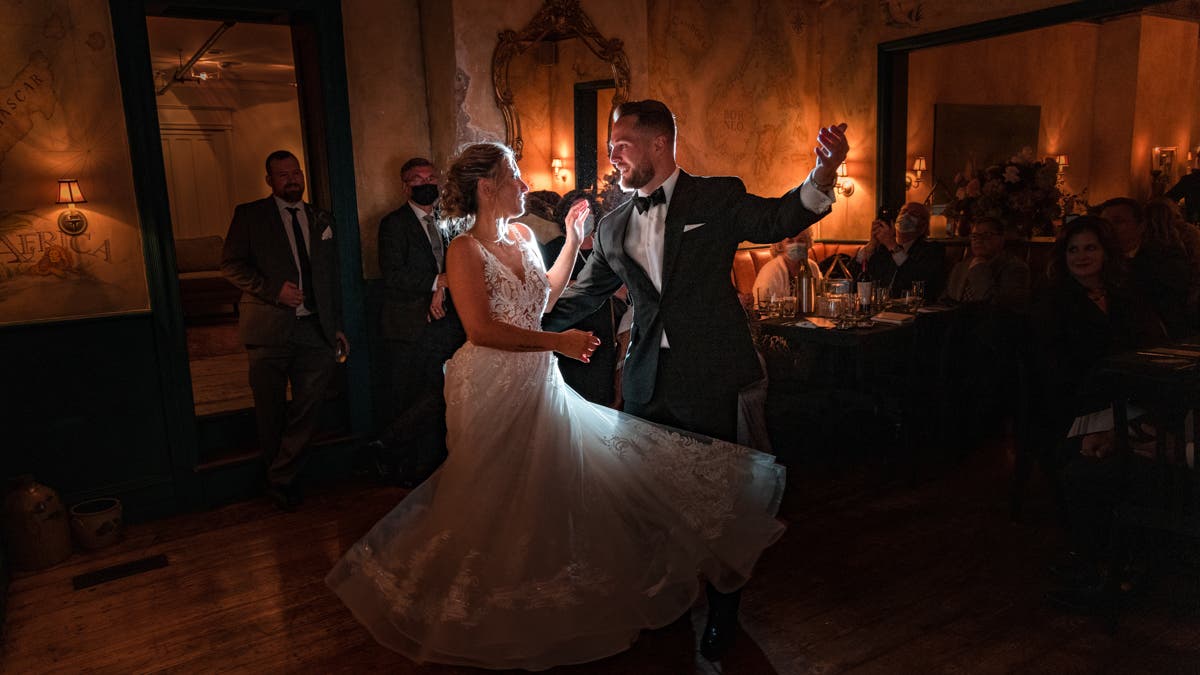 groom in tuxedo and bride in wedding dress happily dance around holding drinks