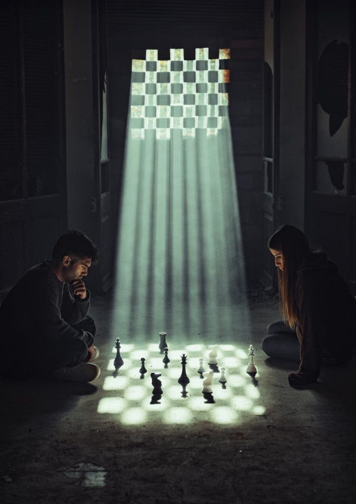 A man and a woman sit facing each other on the floor of a dark, derelict room, deeply focused on a game of chess between them. Strong sunbeams pour down through a checkerboard-patterned window opening behind them, casting a distinct grid of light and shadow over the floor and the chess pieces, mirroring the game board. Created by Jordi Koalitic.