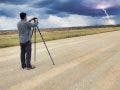 photographer sets up his camera facing a storm in the distance