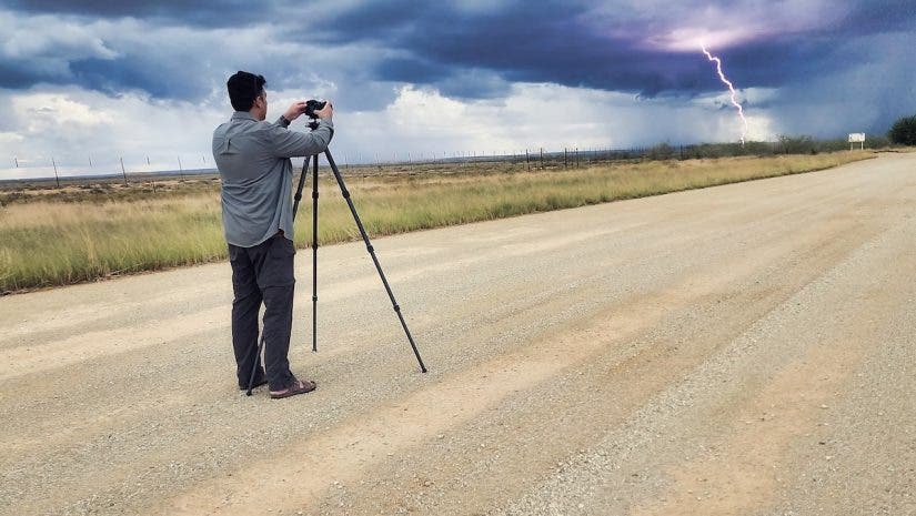 photographer sets up his camera facing a storm in the distance