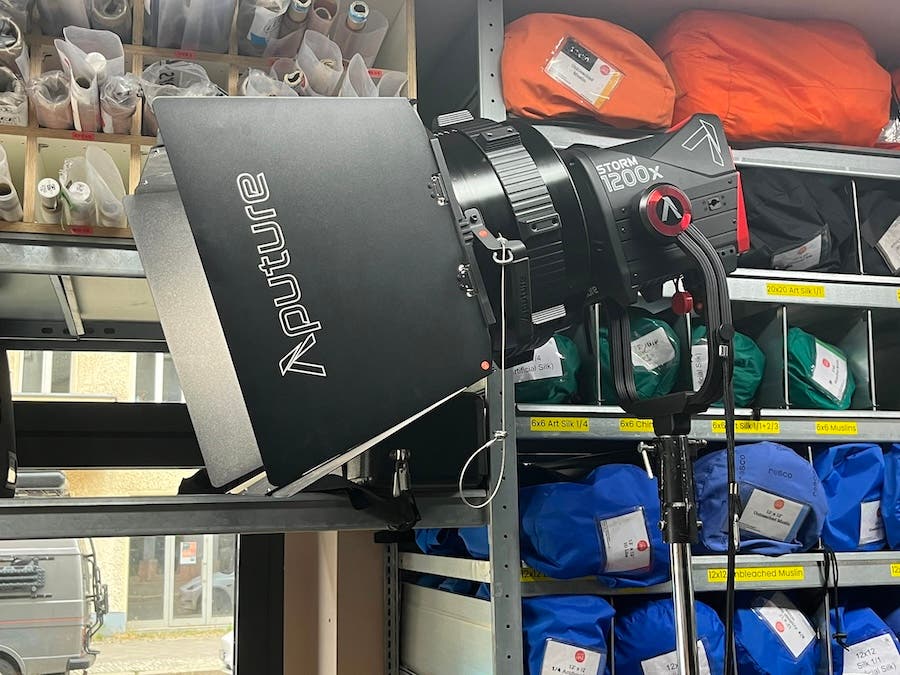 Profile shot of an Aputure STORM 1200x fixture mounted on a light stand equipped with a barn-door attachment inside a studio equipment storage room