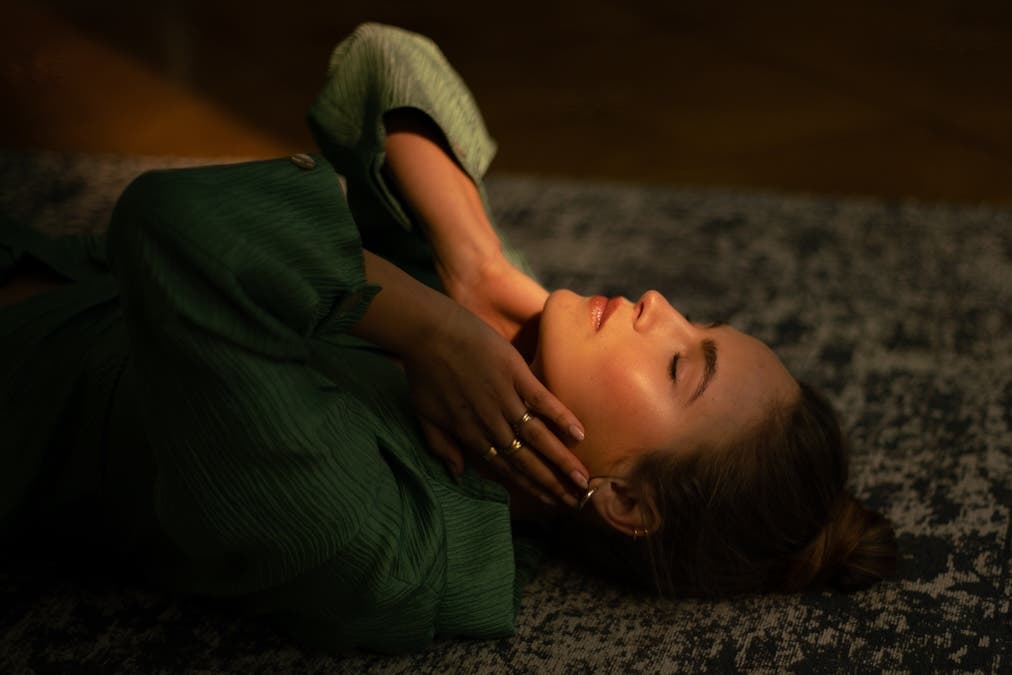 Close-up of a female model lying down on a patterned rug, framed by a soft beam of warm directional light touching her face