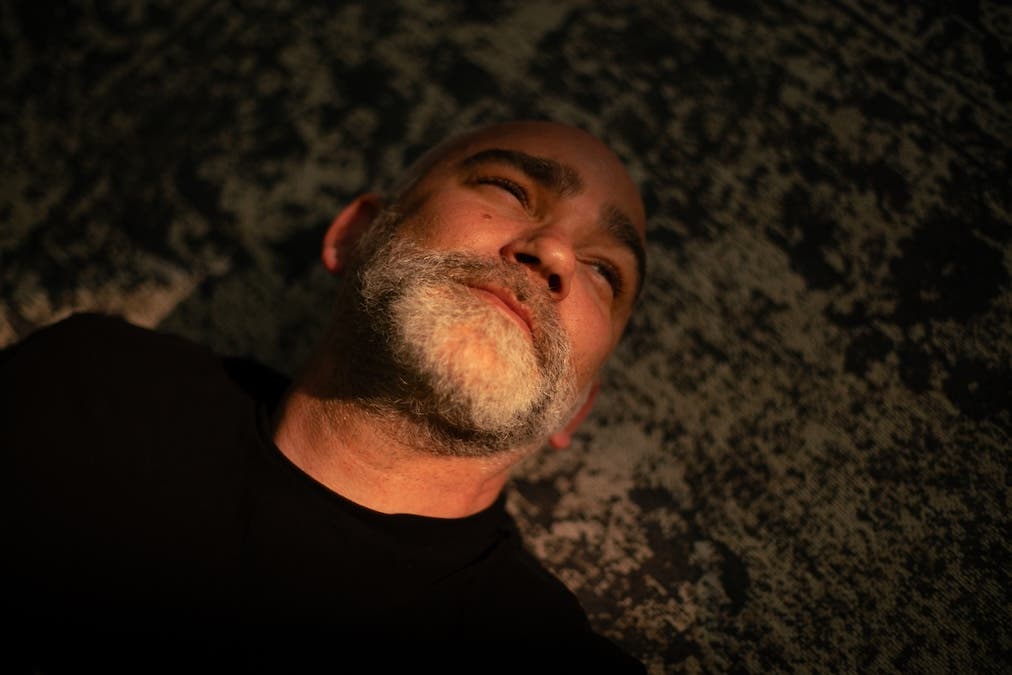 Close-up low-angle shot of a bearded man lying down on a textured carpet with warm light across his face